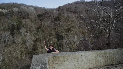 Guy climbs onto stone fence, trying to take selfie in dangerous place 库存影片 113672291