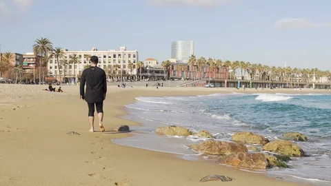 A guy in clothes walking on the shore of a cold and wavy sea in Barcelona Stock Footage 101269739