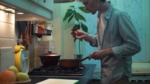 Guy cooking dinner in pot on stove in kitchen. stirs wooden spoon Stock Footage 83049693