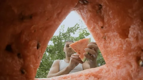 The guy cuts off a piece of watermelon with a knife and immediately eats it. Stock Footage 159154290