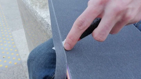 Guy cuts the surface of the skateboard with a knife Video stock 80554204