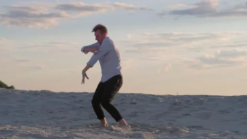 Guy dancing contemporary choreography on the sand at sunset. Slow motion Stock Footage 135611597