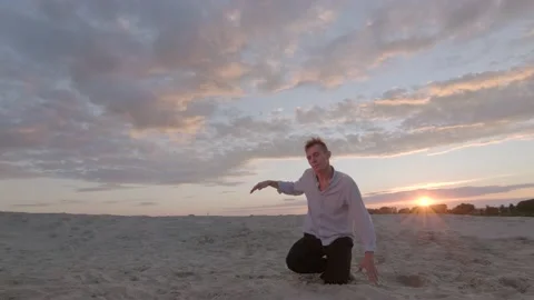 Guy dancing freestyle dance on the sand at sunset. Slow motion. Gimbal shot Stock Footage 135610672