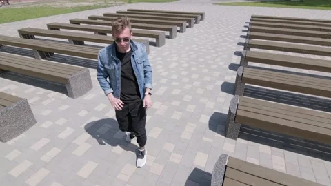 Guy dancing street modern dance in a park between rows of benches. Slow motion Stock Footage 132659772