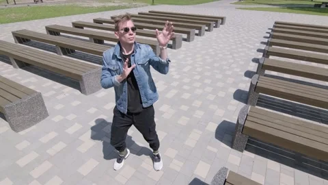 Guy dancing street modern dance in a park between rows of benches. Slow motion Stock Footage 132659838