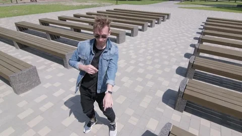 Guy dancing street modern dance in a park between rows of benches. Slow motion Stock Footage 132659844
