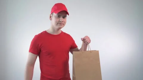 Guy from the delivery service in a bright red T-shirt and cap holds a parcel Stock Footage 131952489