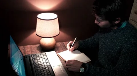 The guy at the desk with a laptop writes in a notebook pen Stock Footage 56250483