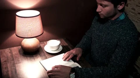 The guy at the desk reading a book and drinking coffee Video stock 56250660