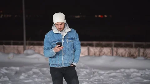 The guy is digging in the phone, and it is snowing around. Stockbeeldmateriaal 147070962