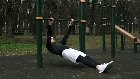 A guy does an Austrian pull-up exercise on a sports field on the street Stock Footage 237989016