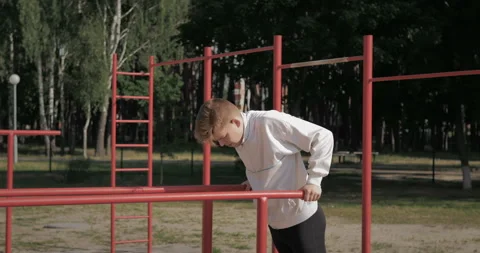 The guy does push-ups on the uneven bars on the street playground.  Stock Footage 135345494