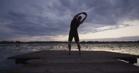 A guy does sports stretching on the river bank at sunset Stock Footage 211904078