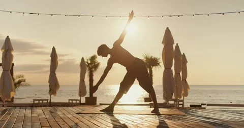 The guy does stretching and stretches to his feet on a sunny beach in the Stock Footage 249235027