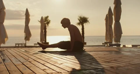 The guy does yoga exercises on a sunny beach in the morning, flooring with Stock Footage 249844194