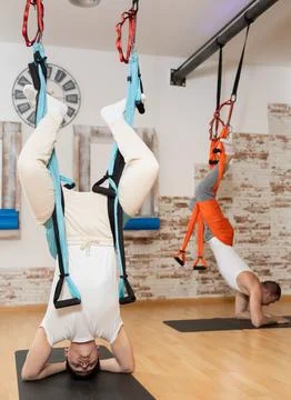 Guy doing handstand supported by suspended hammock in aerial pilates studio Stock Photos
