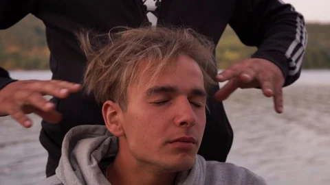 The guy is doing a head massage on the river bank Stock Footage 114631203