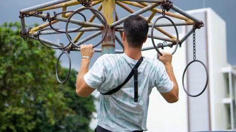 Guy doing a pull-up in a street workout, with building in the background Stock Photos
