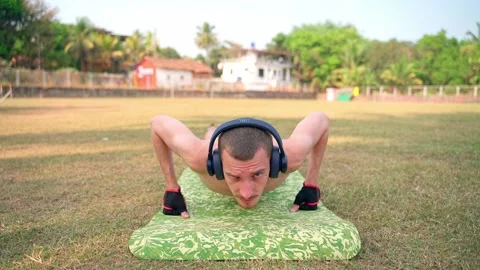 A guy is doing push-ups off the floor. He looks at the camera. Video stock 231336512