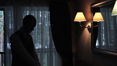 The guy dresses in the mirror, straightens his shirt. The silhouette of a man. Vidéo 106576948
