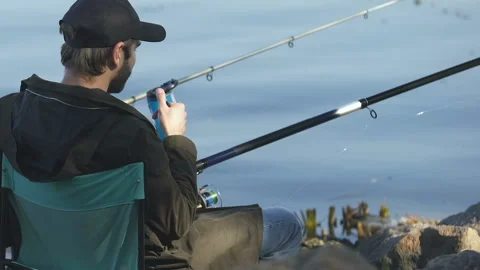 Guy drinking beverage from thermo cup, holding fishing rod, angling activity Video stock 99844343