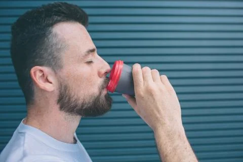 Guy is drinking coffee from plastic cup. He is keeping eyes closed. Isolated  Photos