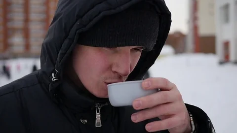 The guy is drinking hot tea from a mug in the winter outdoor. Closeup Vidéo 70062419