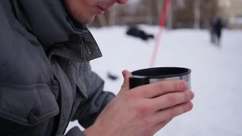 The guy is drinking hot tea from a mug in the winter outdoor. ice rink Vidéo 70443077