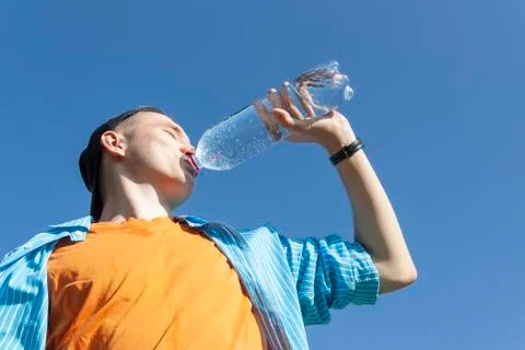 Guy drinking water from a bottle against a blue sky Stock Photos