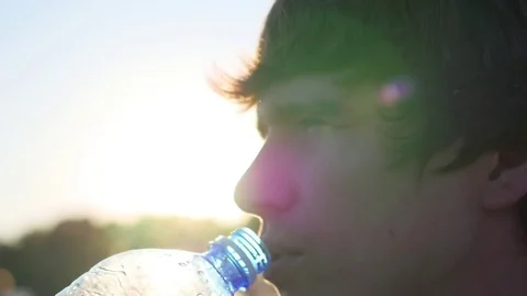 Guy drinks water from the bottle at sunset Video stock 76884430