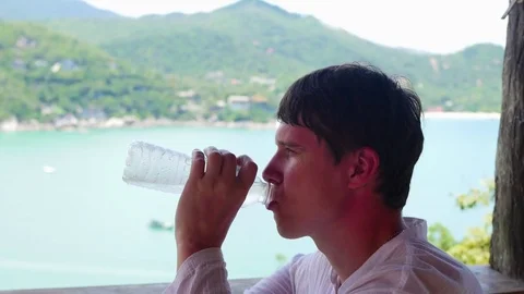 The guy drinks water on a hot day. Panoramic view of the sea and mountains Vidéo 74762839