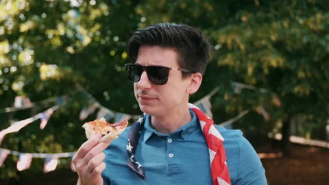 Guy eating a slice of pizza while nodding along outdoors Stock Footage 133629832