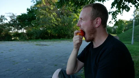 The guy eats fruit in the summer park Stock Footage 114821659