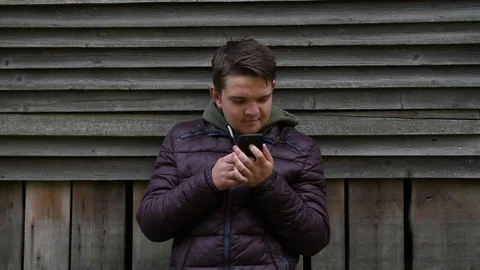 Guy emotionally looking at something on phone against wooden wall background Stock Footage 129684253