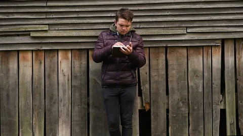 Guy emotionally writes something in a notepad on a background of a wooden wall Stock Footage 129684302