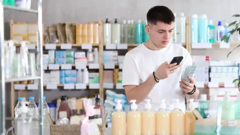 Guy of European appearance scans the barcode of a package with moisturizer on Stock Footage 331296222
