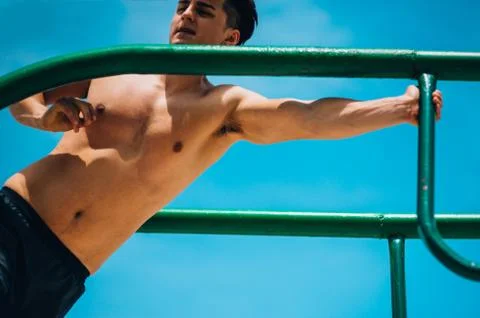 Guy exercising arms doing hard exercises on metal bars 库存照片