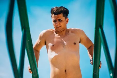 Guy exercising arms doing hard exercises on metal bars 库存照片