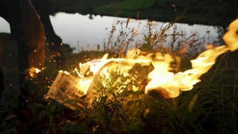The guy extinguishes a burning newspaper lying in the grass with his feet Stock Footage 138143049