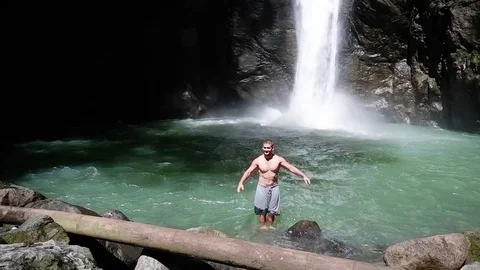 Guy falls backwards into a large beautiful waterfall. Video stock 122965664