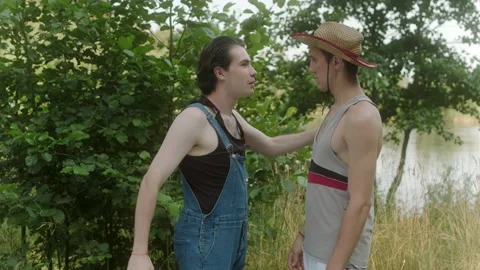 A guy in a farm jumpsuit puts a straw hat on a guy in a T-shirt Stock Footage 197481864