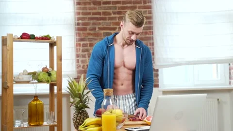 Guy fitness trainer, bodybuilder preparing fruit salad online in front of laptop Stock Footage 143753141