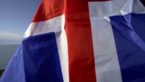 A guy with the flag of Iceland is standing on the edge of a cliff.Cape Dyrholaey Stock Footage 130443443