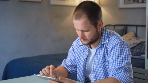 The guy flips through the news on a digital tablet and looks at the camera Stock Footage 128551541