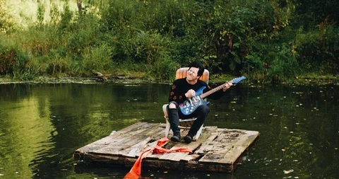 The guy floats on a raft on the pond and plays the guitar.Cool cool shots Stock Footage 114520440