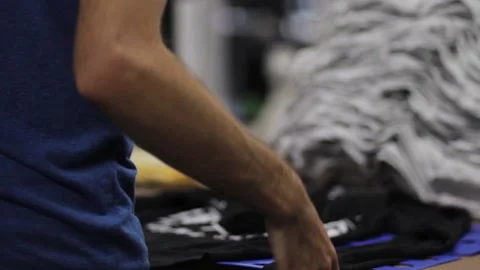 Guy folding shirts at a screen printing or retail business Stock Footage 139387178