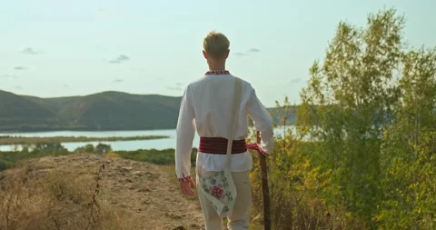 Guy in a folk costume and with a staff in his hands is walking along a mountain Stock-Footage 144642353