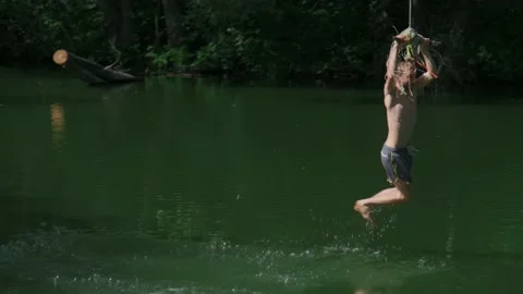 The guy in the forest rides over the water bungee on a tree, jumps into the lake Stock Footage 198050987