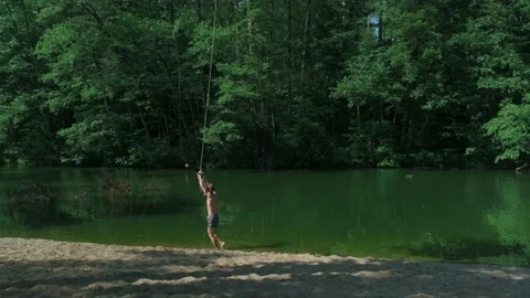 The guy in the forest rides over the water bungee on a tree, jumps into the lake Stock Footage 198051550