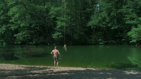 The guy in the forest rides over the water bungee on a tree, jumps into the lake Stock Footage 198051628